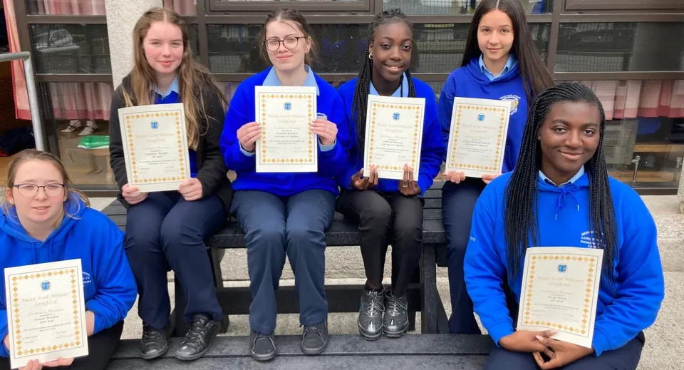 Studenti della Meán Scoil Mhuire di Longford posano in divisa blu con attestati davanti a un edificio in mattoni.