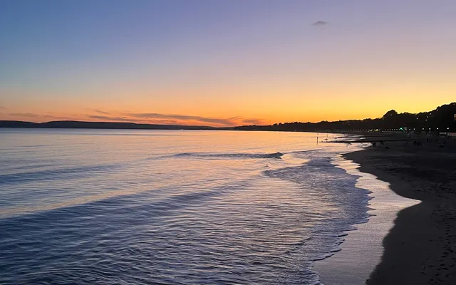 Playa al atardecer con el mar en calma y el cielo naranja