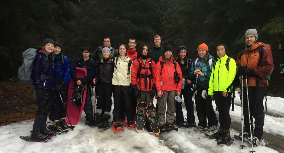 Un gruppo di studenti della Keystone School si trova in un bosco innevato indossando abiti invernali colorati.