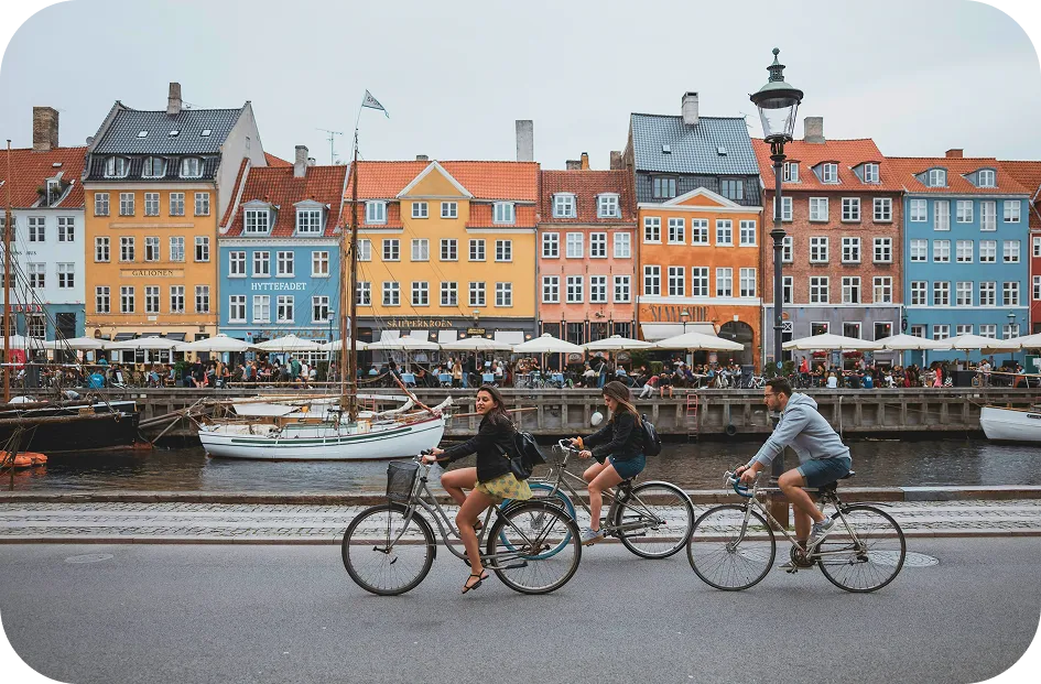 Tre persone in bicicletta davanti alle case colorate di Nyhavn a Copenhagen