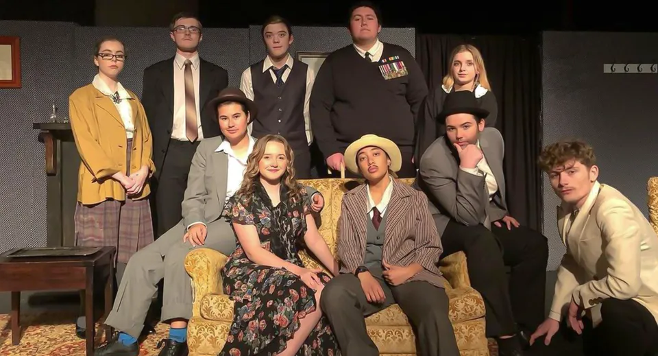 Un gruppo di studenti dell'Upper Hutt College in abiti formali sul palco con elementi di scena sullo sfondo.