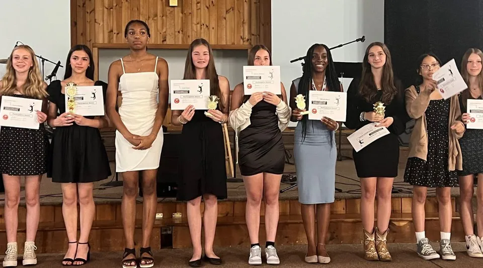 Un gruppo di studentesse della Harmony Christian School tiene ciascuna in mano un attestato all'interno di una stanza in legno.