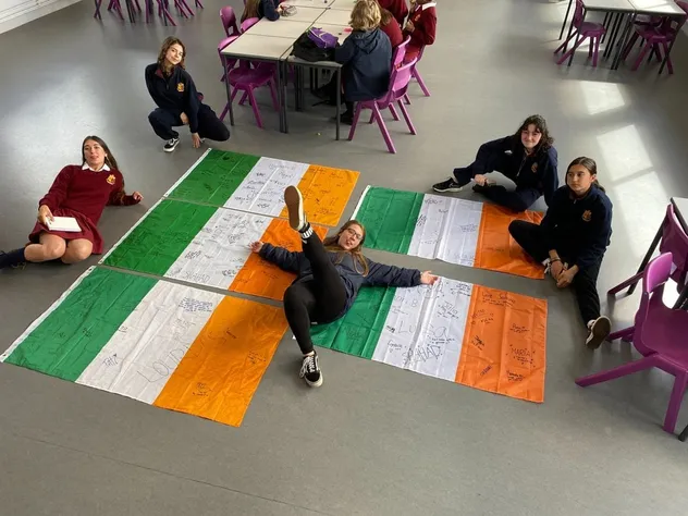 Austauschschüler sitzen um eine große irische Flagge auf dem Schulboden