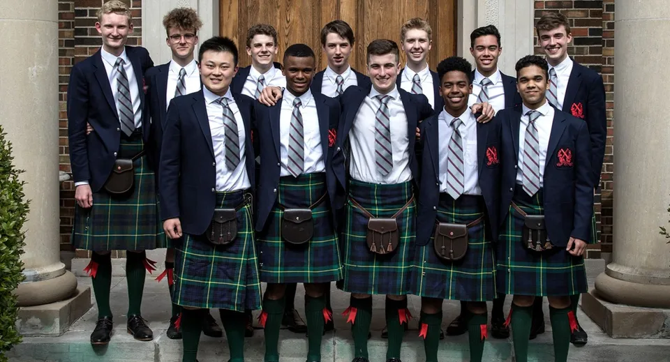Un gruppo di studenti in abito formale davanti a una porta di legno nel campus del St. Andrew’s College.