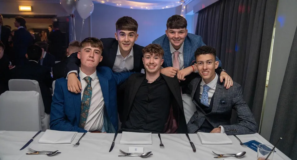 Un gruppo di studenti della Loughborough Grammar School posa in abito formale durante un evento con una tenda sullo sfondo.