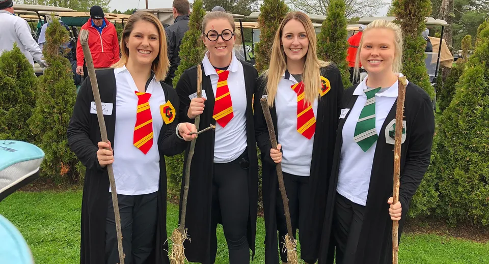 Quattro studentesse della Lambton Kent Composite School indossano tuniche e sciarpe in stile Hogwarts all'aperto davanti ad alberi ed edifici.