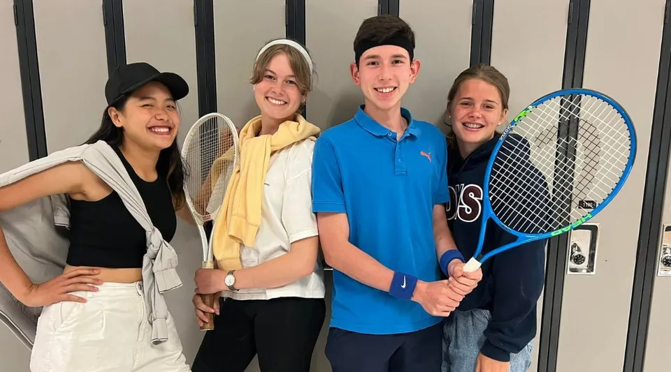Un gruppo di quattro studenti della Rockland District High School davanti a un campo da tennis con le racchette da tennis in mano.
