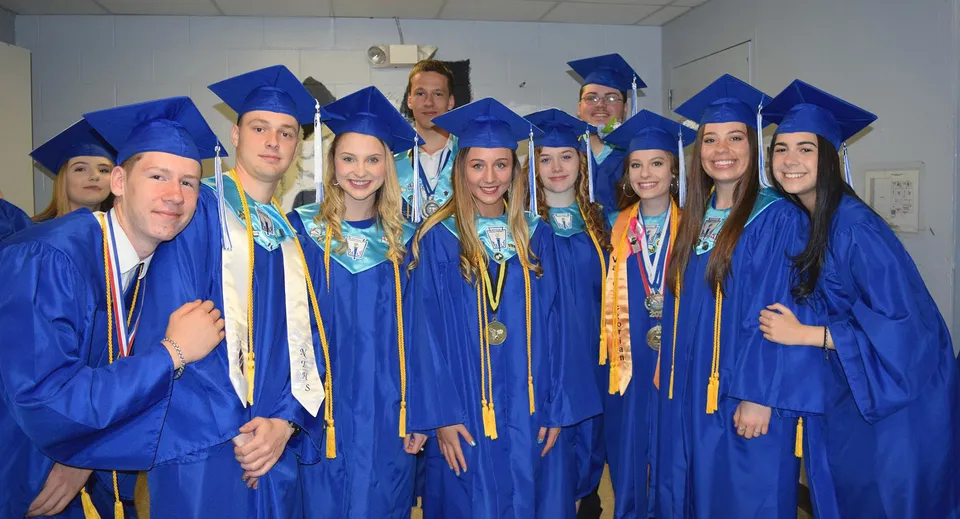 Un gruppo di diplomati in toga blu festeggia il proprio diploma in un'aula della Lee Academy.