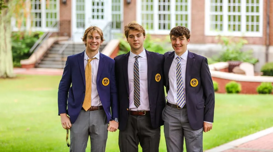 Tre studenti della Trinity-Pawling School sono insieme sul campus erboso davanti a un edificio scolastico.