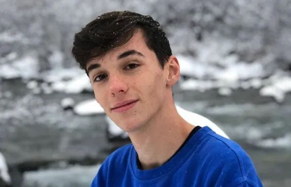 Estudiante con camiseta azul y copos de nieve en el pelo junto a un río helado