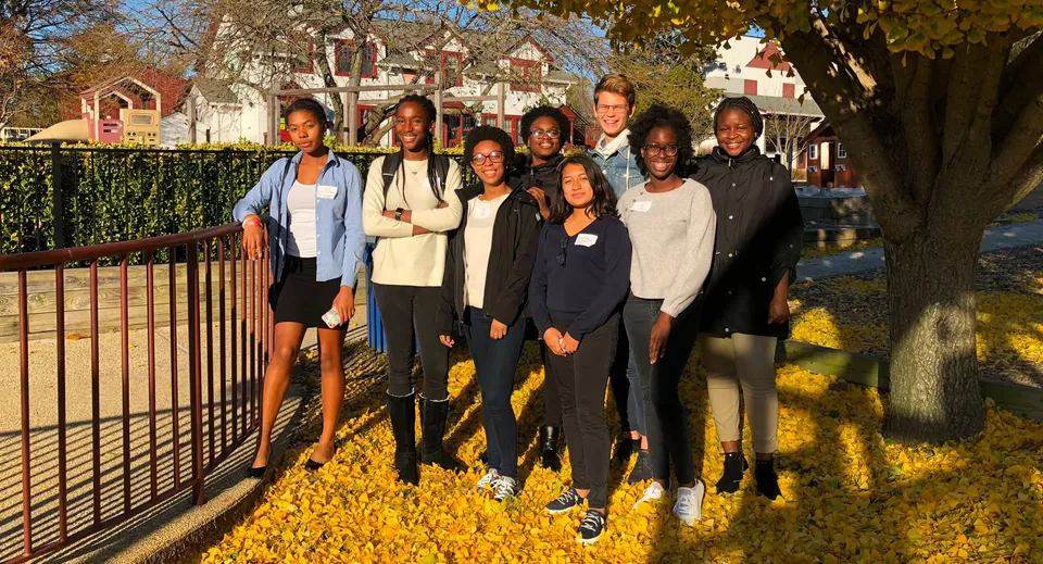 Un gruppo di studenti e adulti si trova all'aperto davanti a un fogliame autunnale colorato nel campus della West Nottingham Academy.