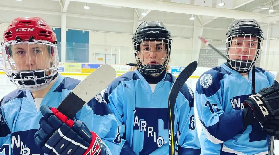 Tre giocatori di hockey in divisa blu sono in piedi sulla pista da ghiaccio al coperto della Tagwi Secondary School.