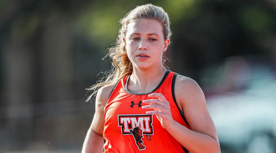 Una studentessa della TMI Episcopal in maglia sportiva rossa si trova all'aperto davanti a uno sfondo sfocato con alberi.