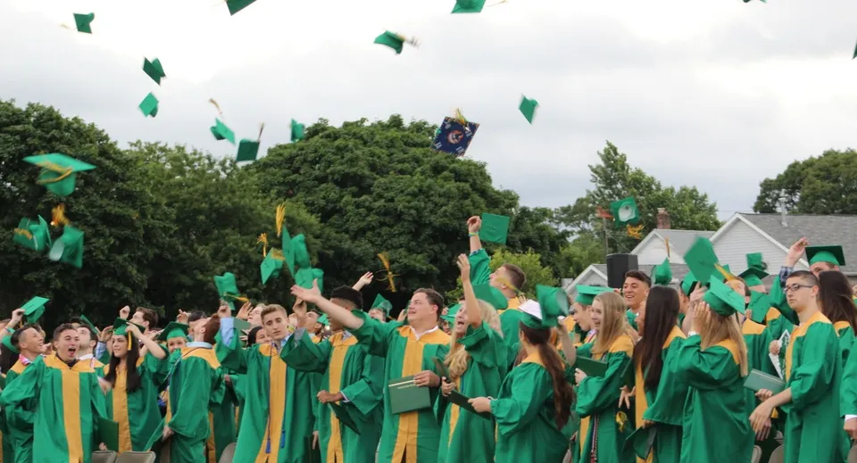 Un grande gruppo di diplomati in toga verde e gialla all'aperto nel campus della Oakland Christian School.