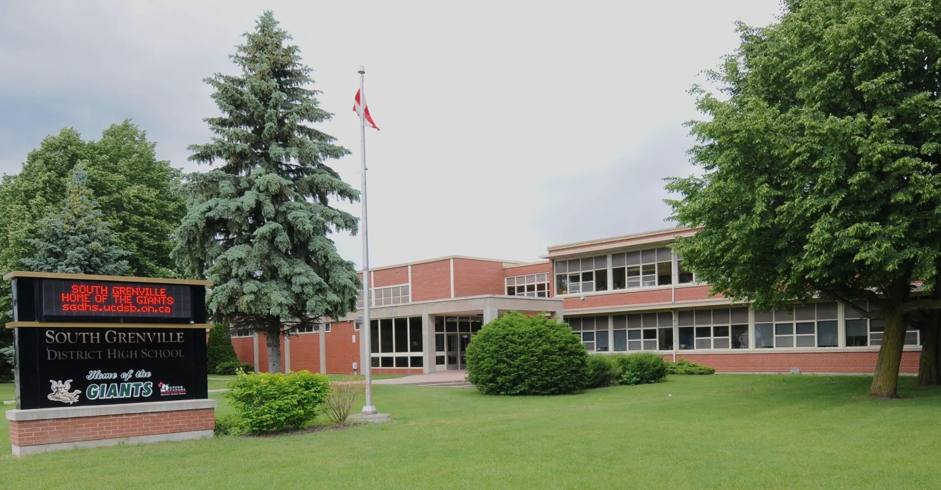 L'edificio in mattoni della South Grenville District High School con una bandiera canadese e circondato da alberi e prato.