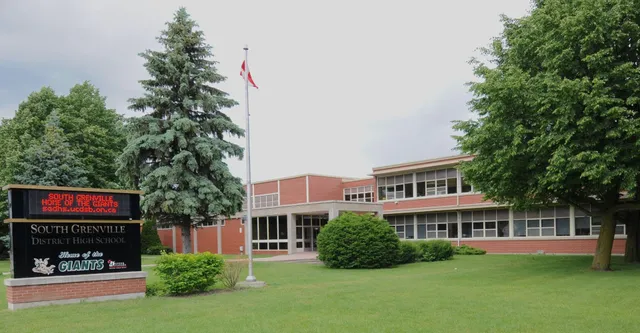 L'edificio in mattoni della South Grenville District High School con una bandiera canadese e circondato da alberi e prato.