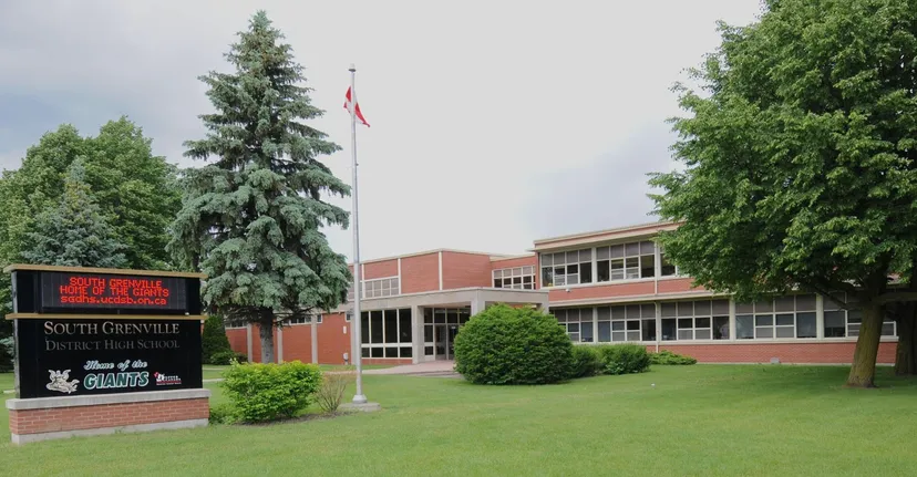 L'edificio in mattoni della South Grenville District High School con una bandiera canadese e circondato da alberi e prato.
