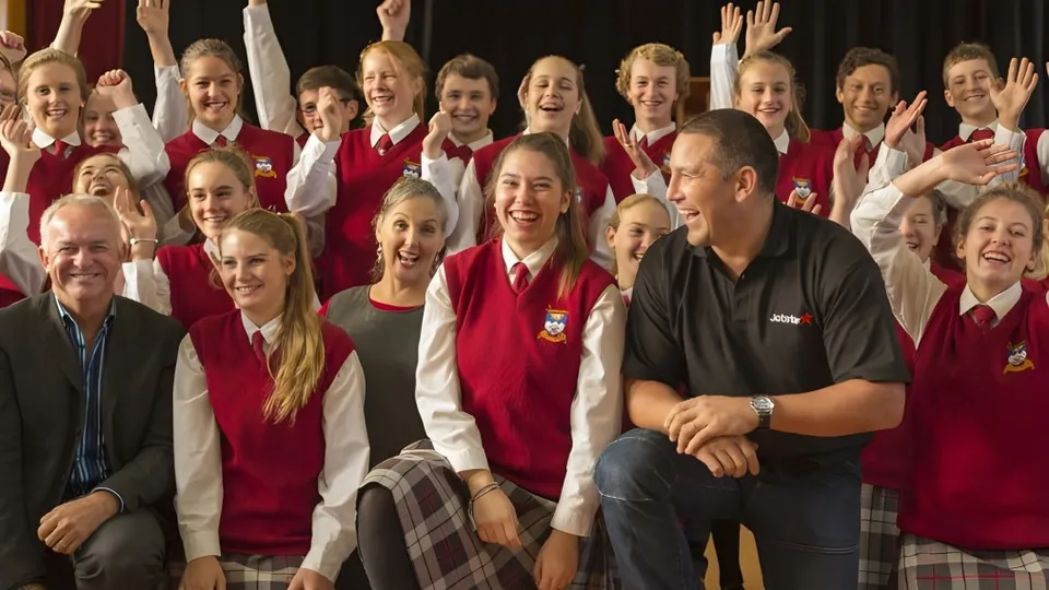 Studenti della Dunstan High School in divisa scolastica rossa esultano e sorridono insieme ad alcuni adulti.