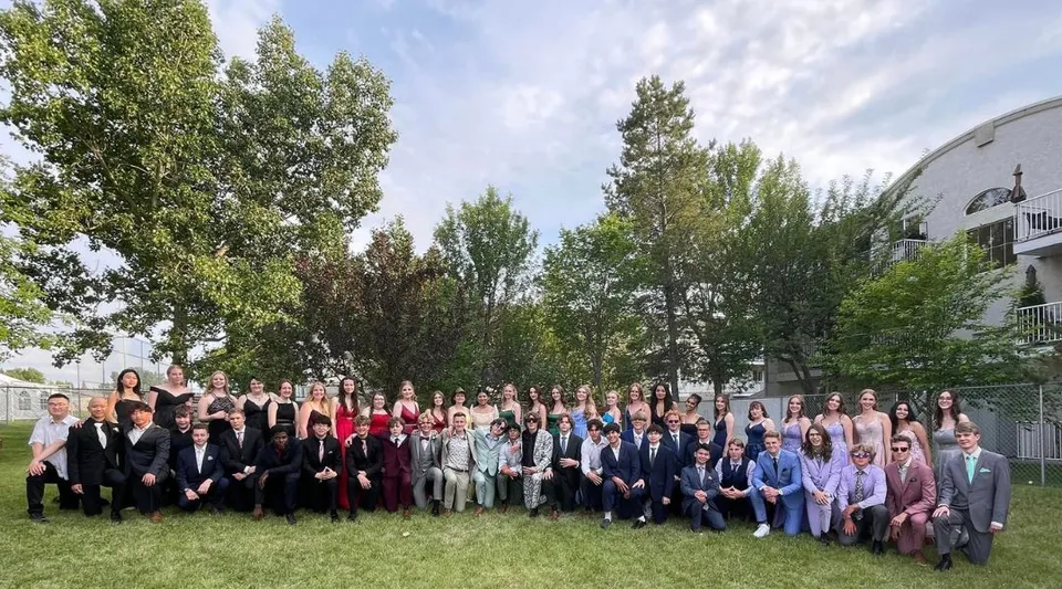 Un grande gruppo di studenti della Calgary Christian School si raduna all'aperto davanti a un edificio con alberi sullo sfondo.