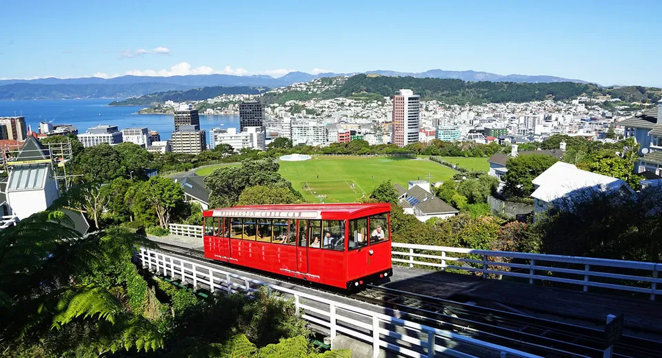 Una funivia rossa nel campus del Scots College offre una vista panoramica della città con grattacieli e montagne sullo sfondo.