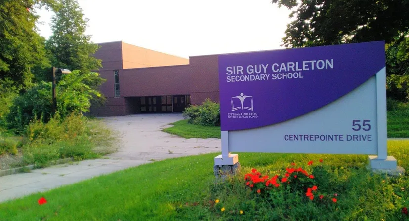 L'ingresso della Sir Guy Carleton Secondary School con una grande insegna e un prato fiorito ben curato in primo piano.