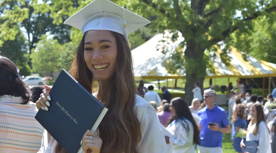Una diplomata della Linden Hall indossa tocco e toga e tiene in mano il suo diploma durante la cerimonia di diploma all'aperto.