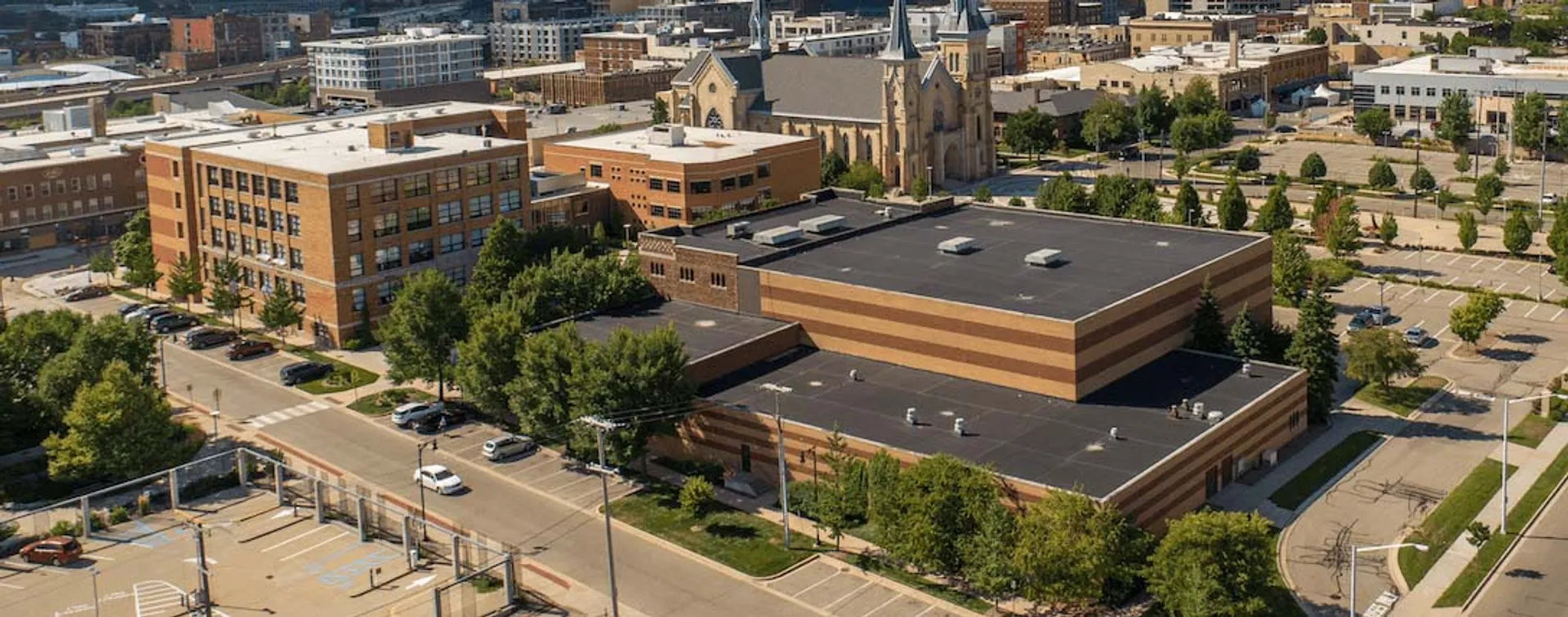 L'edificio principale della Catholic Central High School è circondato da alberi e fa parte di uno skyline cittadino con edifici moderni e storici.