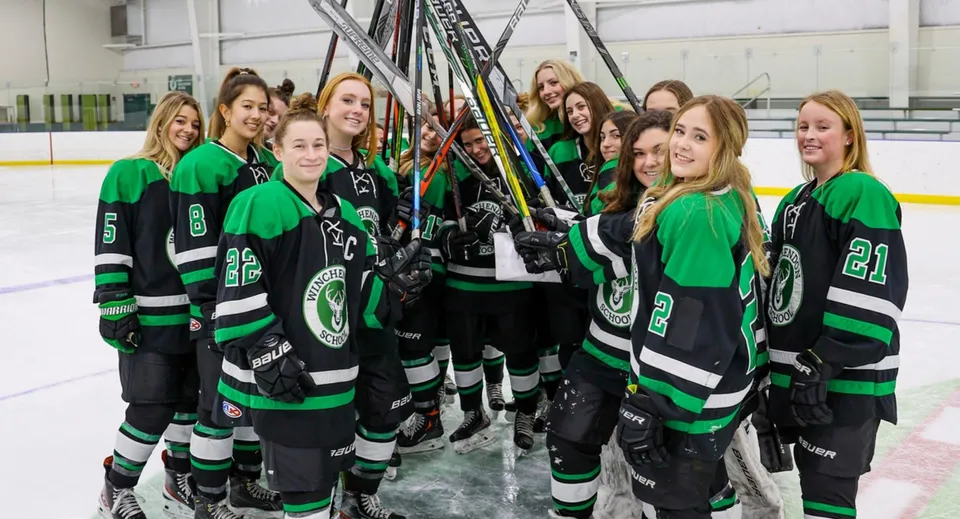 Un gruppo di giovani giocatrici di hockey con maglie verdi e nere sul ghiaccio della Winchendon School in Massachusetts.