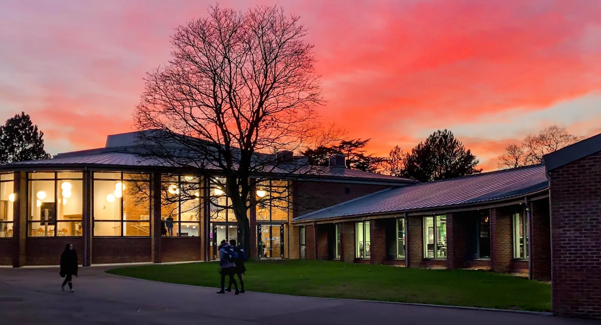 L'edificio illuminato della Leighton Park School davanti a un cielo rosso al tramonto con un albero privo di foglie.