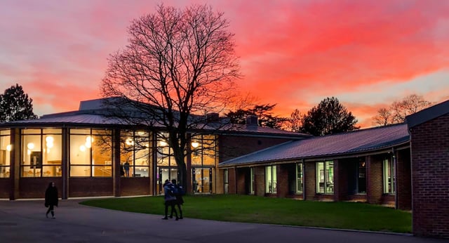 L'edificio illuminato della Leighton Park School davanti a un cielo rosso al tramonto con un albero privo di foglie.