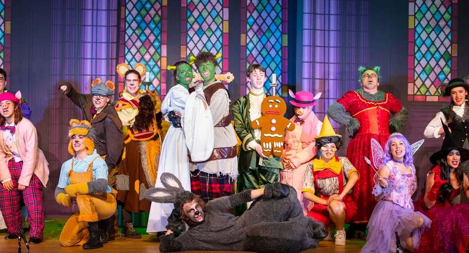 Studenti della ACS International School Cobham mettono in scena un variopinto spettacolo teatrale davanti a uno sfondo con vetrata della chiesa.