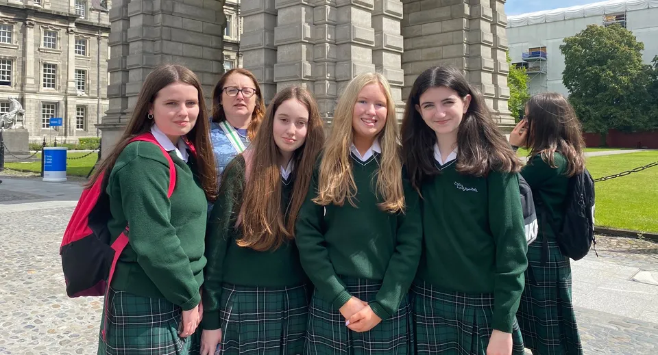 Un gruppo di studentesse della St. Louis Secondary School in divisa scolastica davanti a un edificio storico con un'area verde sullo sfondo.