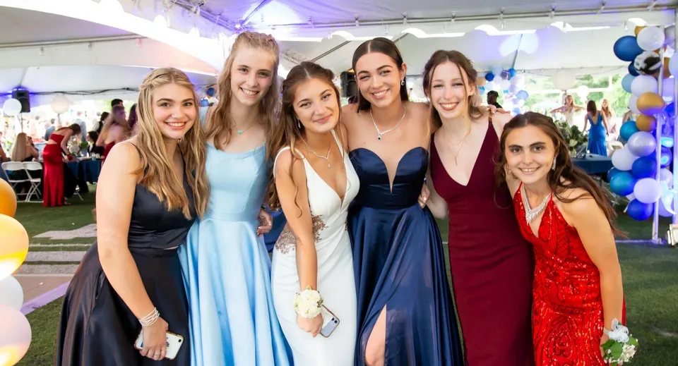 Un gruppo di giovani donne in abiti eleganti posa all'aperto nel campus della Earlscliffe School con palloncini sullo sfondo.