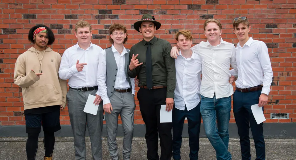 Un gruppo di studenti si trova davanti a un muro di mattoni nel campus del Taupo-nui-a-Tia College.