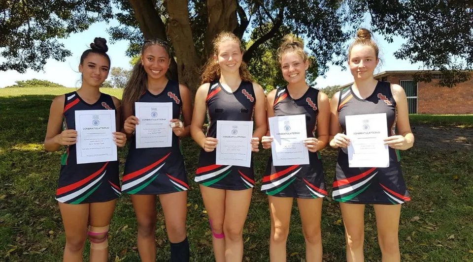 Un gruppo di giovani atlete tiene in mano dei certificati davanti a un bosco presso la South Sydney High School.