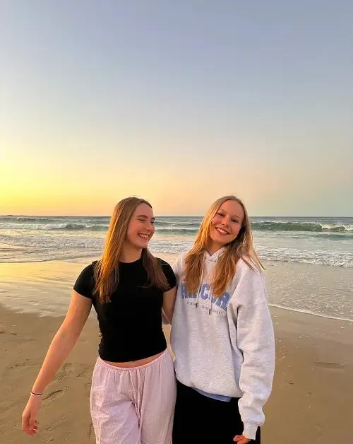 Due studentesse sorridenti passeggiano sulla spiaggia al tramonto in Australia
