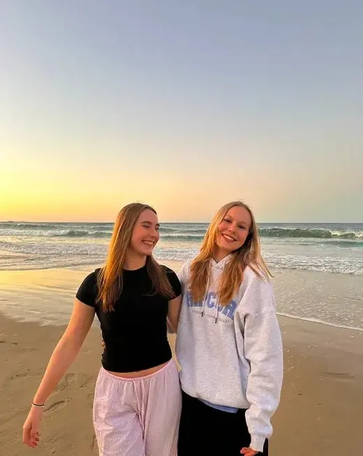 Due studentesse sorridenti passeggiano sulla spiaggia al tramonto in Australia