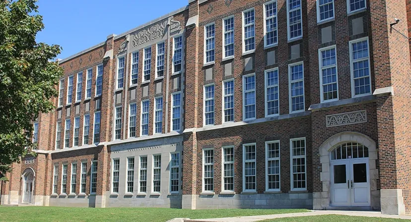 L'edificio in mattoni a più piani del London South Collegiate Institute, con molte finestre e un ingresso ad arco, è circondato da alberi.