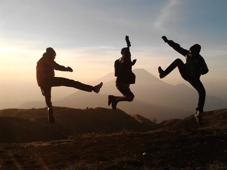 Silhouetten von drei Jugendlichen, die vor Bergen im Gegenlicht in die Luft springen