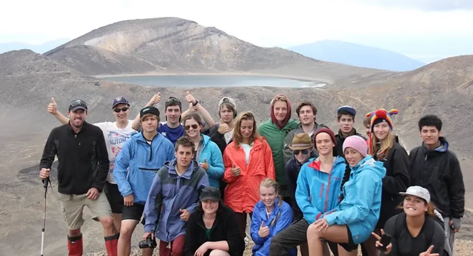 Un gruppo di studenti della Freyberg High School posa davanti a un suggestivo paesaggio montano con lago.
