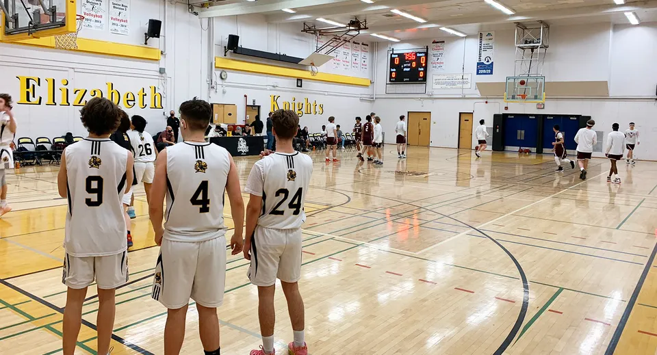 Un gruppo di giovani giocatori di basket si trova sul campo da basket nella palestra della Queen Elizabeth High School.
