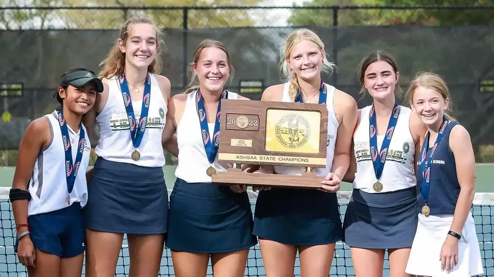 Sei tenniste della Hayden Catholic High School posano con medaglie e un trofeo accanto alla rete da tennis.