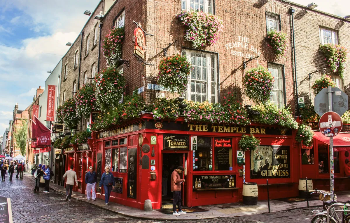Fachada roja del pub The Temple Bar en Dublín, decorada con flores, y gente paseando por la calle