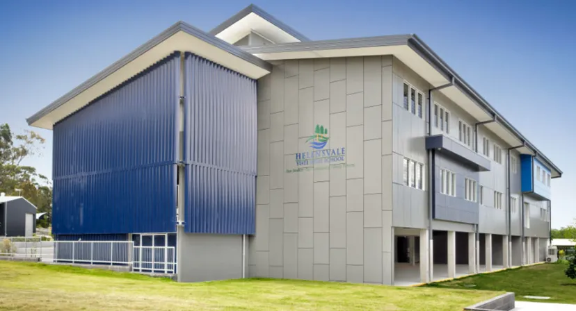 L'edificio moderno a più piani della Helensvale State High School con pannelli esterni grigi e blu e un prato in primo piano.