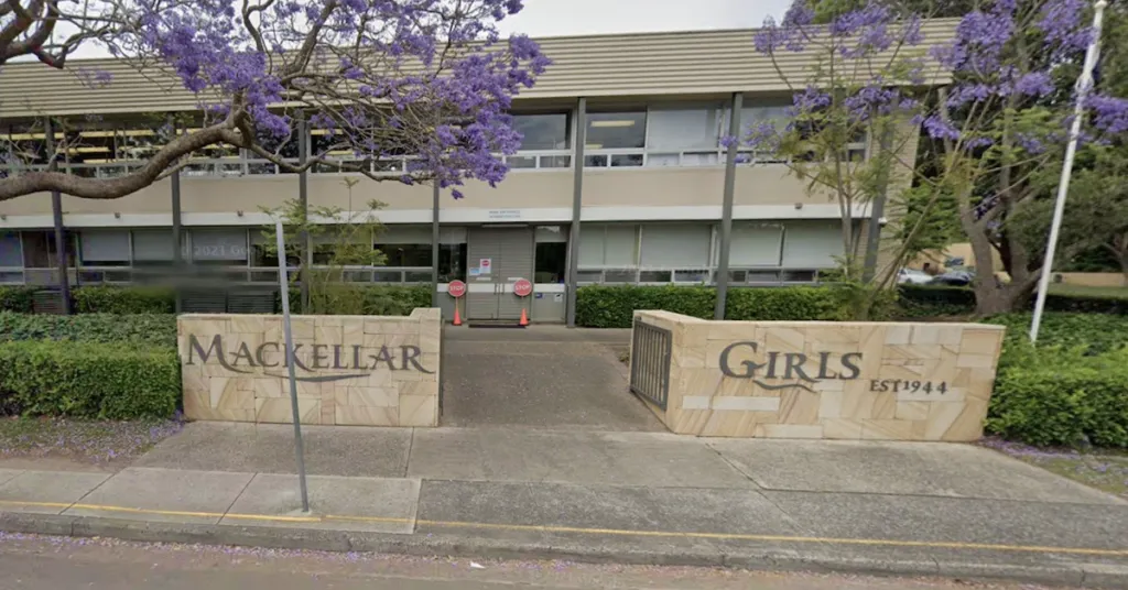 El edificio con el cartel Mackellar Girls Campus está rodeado de árboles con flores violetas.