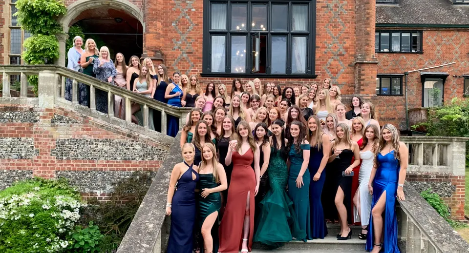 Un gruppo di giovani donne in abito formale si trova davanti a un edificio storico in mattoni nel campus del Shiplake College.