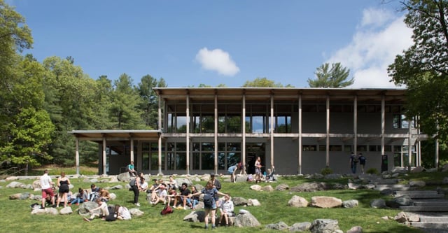 Schüler sitzen und stehen auf einer Wiese vor dem modernen Holz- und Glasgebäude der The Cambridge School of Weston.