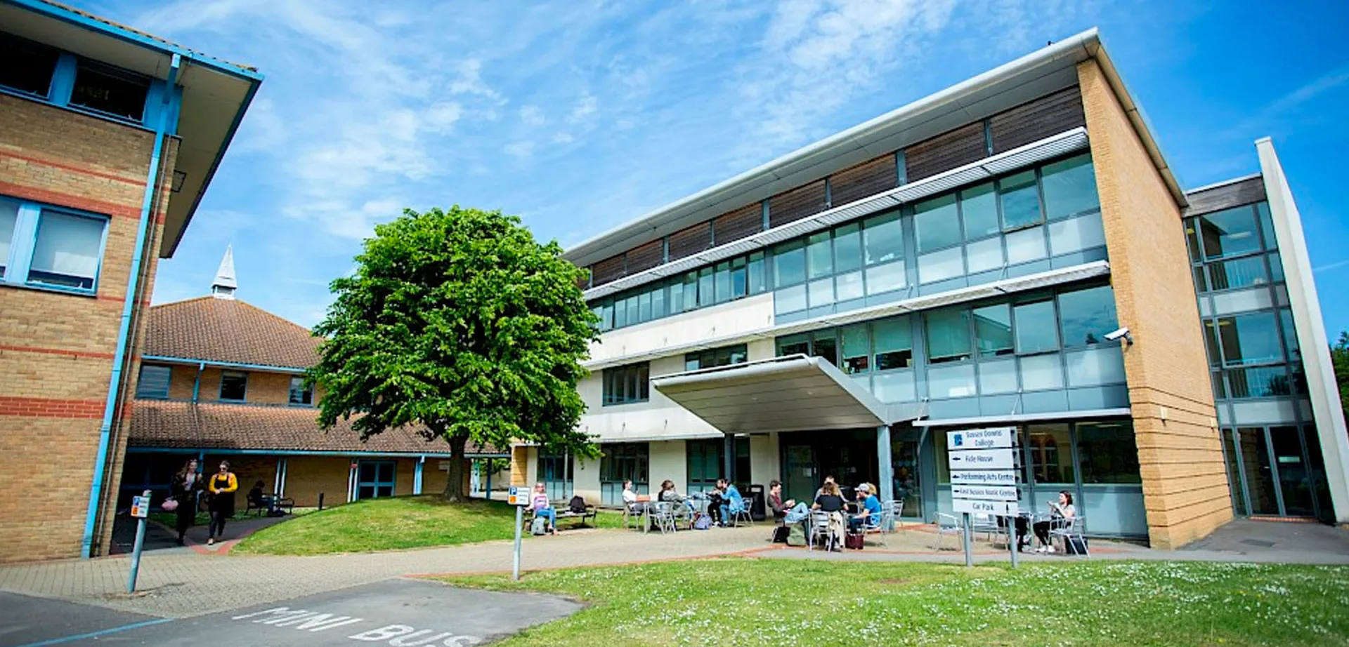 L'edificio moderno dell'East Sussex College Lewes con un cortile dove alcuni studenti siedono a tavoli all'aperto.