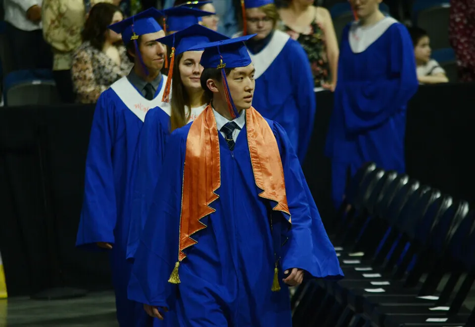 Un gruppo di diplomati in toga blu e arancione si trova a una cerimonia di diploma della Winston Churchill High School.