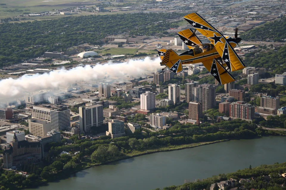 Un aereo acrobatico esegue manovre acrobatiche sopra lo skyline con grattacieli e acqua sullo sfondo sul campus della Holy Cross High School.